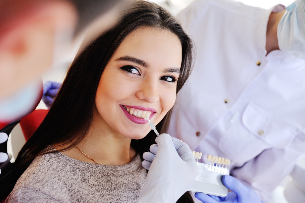 Woman smiling while dentist compares veneer colors to her teeth color